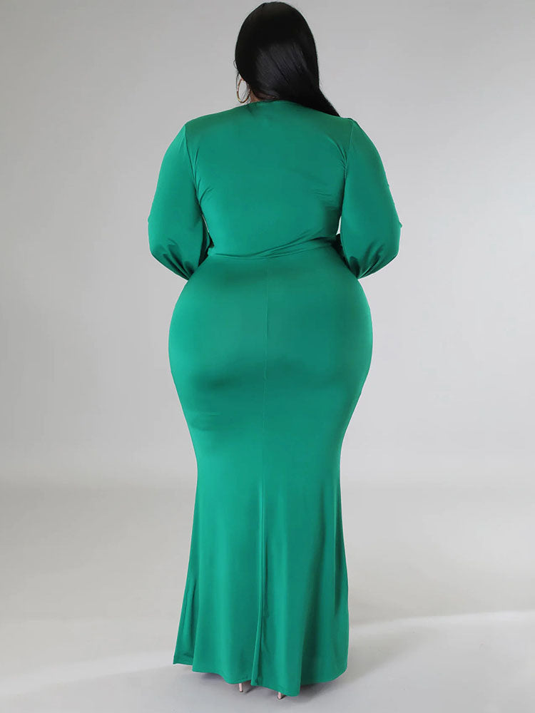 Back view of a woman wearing a green, floor-length, long-sleeved gown with a V-neckline and draped skirt