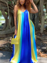 Woman with curly hair wearing a blue, yellow, and white tie-dye maxi dress and a yellow handbag, standing outdoors.