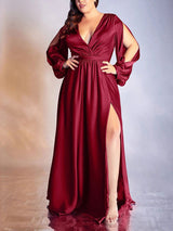 Woman in a burgundy satin maxi dress with a V-neck, cut-out long sleeves, and a high slit, standing with hands on hips.