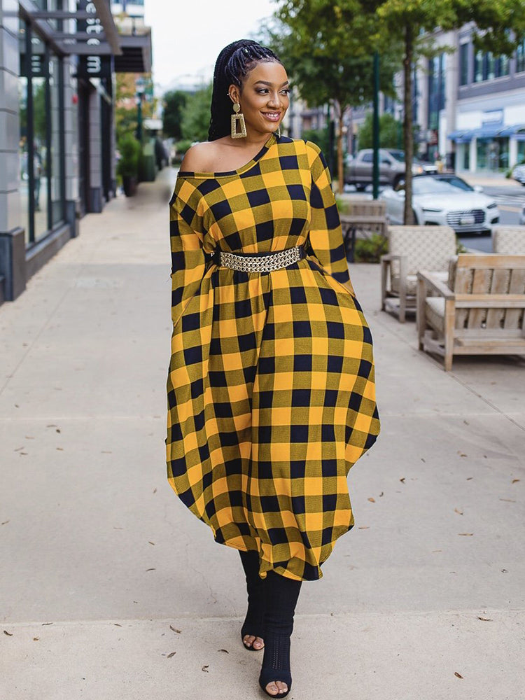 Woman wearing a yellow and black plaid off-the-shoulder midi dress with a gold belt and black boots, walking on a sidewalk.