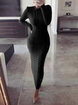 Woman wearing a long black cable knit dress with long sleeves and a mock neck standing in a living room.