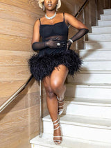 Woman in a black mini dress with feather trim and long gloves, wearing strappy heels and jewelry, standing on stairs.