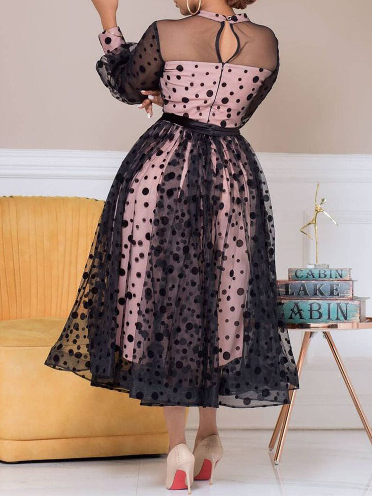Back view of a woman in a pink and black polka dot midi dress with sheer sleeves.