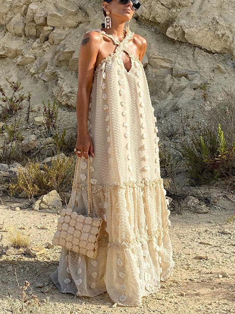 Close-up of the cream-colored maxi dress, highlighting the textured fabric, floral embellishments, and halter neckline.