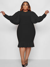 Woman wearing a black dress with puff sleeves and a ruffle hem.