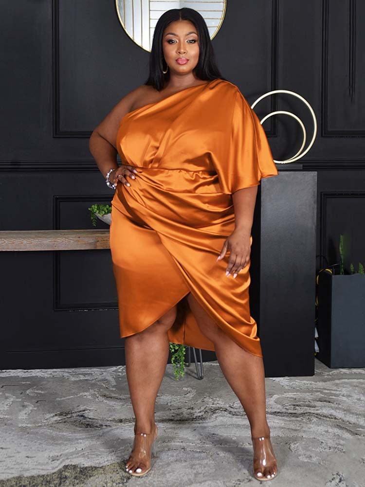 Woman wearing an orange one-shoulder satin dress with draping and a tulip hem, posing with hand on hip.