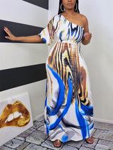 Woman wearing a one-shoulder maxi dress with an abstract print, standing against a striped wall.