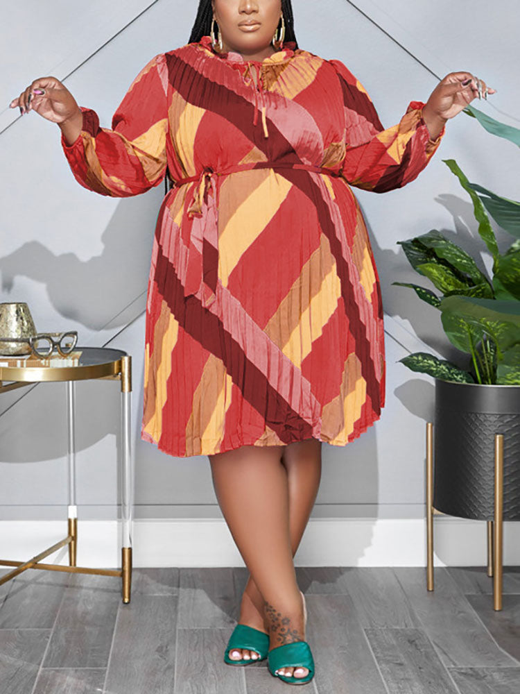 Plus-size woman wearing a warm-toned, long-sleeved, pleated A-line dress with a geometric print and tie-waist.