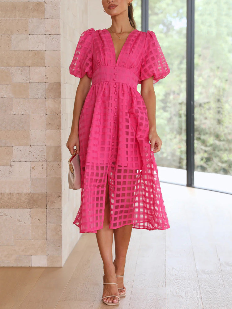 Full body shot of a woman in a hot pink midi dress with a sheer grid overlay, puffed short sleeves, and a button-down front, paired with nude heels and a light pink handbag.