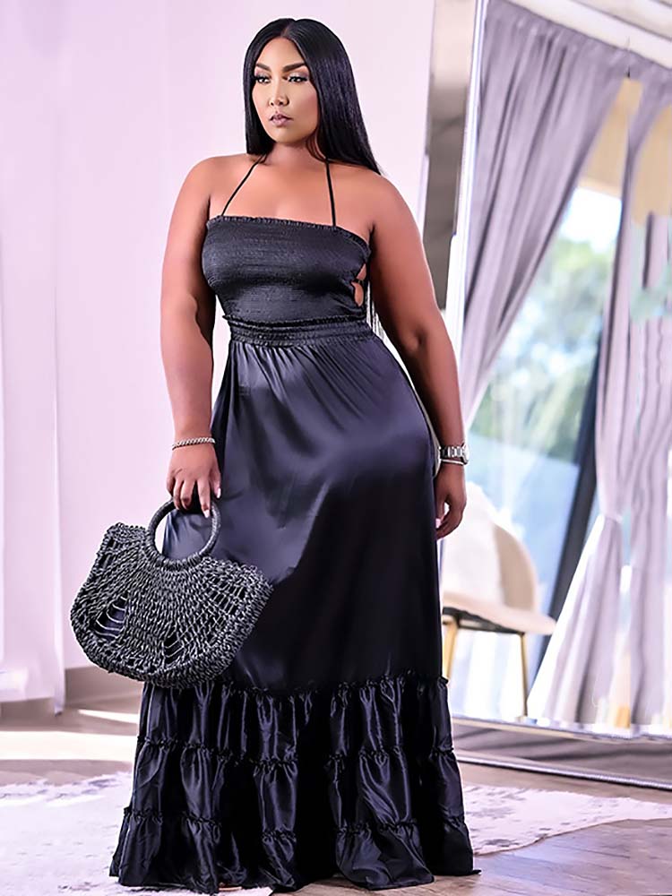 Woman in a black satin maxi dress with a halter neckline and ruffled hem, holding a woven handbag.