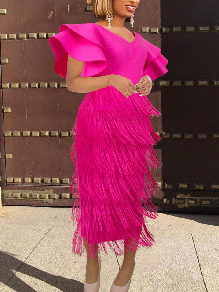 A woman in a fuchsia tiered fringe dress with ruffled sleeves poses in front of a large wooden door.