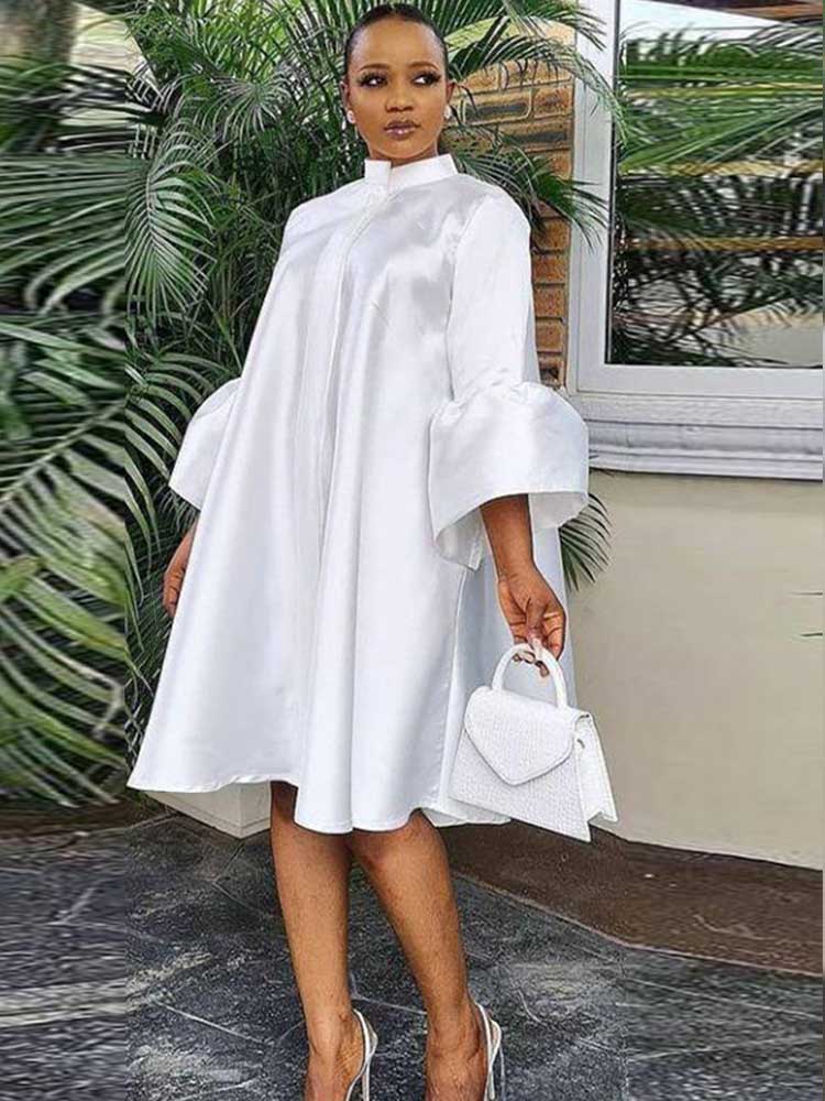 Woman wearing a white A-line dress with bell sleeves and a high neckline, holding a white handbag.