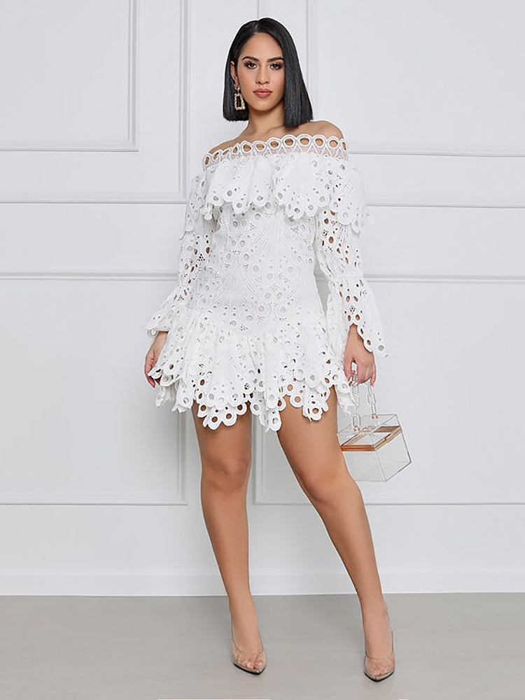 Full body shot of a woman wearing a white off-the-shoulder eyelet lace mini dress with bell sleeves and ruffled tiers, holding a clear handbag and wearing clear heels.