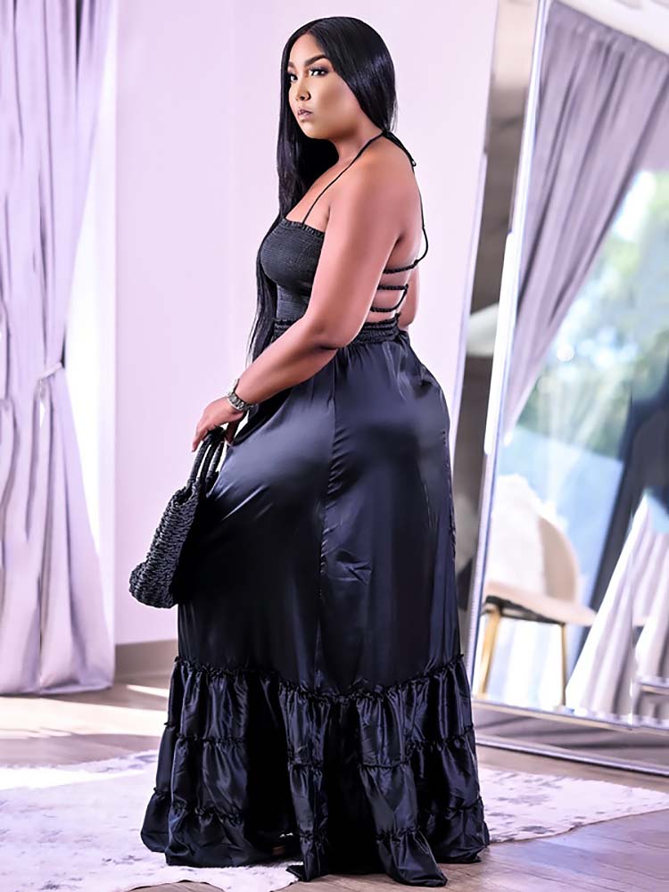 Side view of a woman in a black satin maxi dress with a halter neckline and ruffled hem.