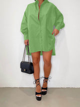 Woman wearing an oversized lime green collared shirt dress with a high-low hemline, paired with black platform heels and a black quilted handbag.
