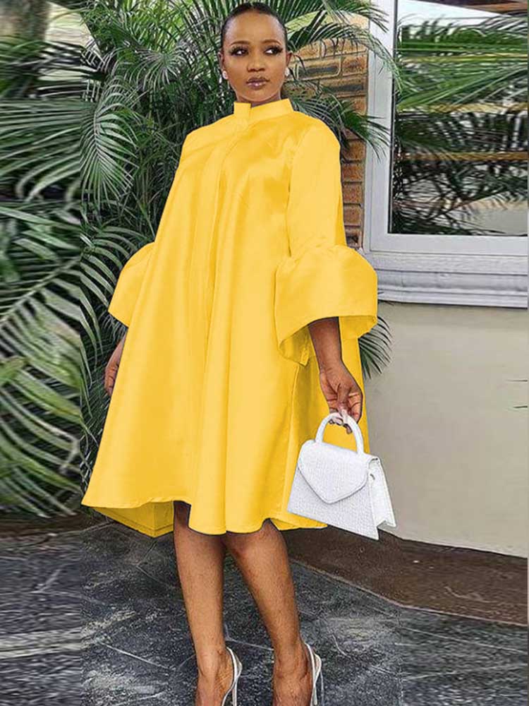 Woman wearing a yellow A-line dress with bell sleeves and a high neckline, holding a white handbag.
