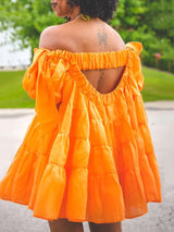 Back view of a woman wearing an orange off-the-shoulder tiered mini dress with an open back.