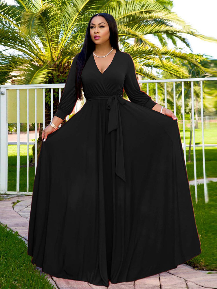 Woman wearing a long black wrap dress with a V-neck and long sleeves, standing outdoors with palm trees in the background.