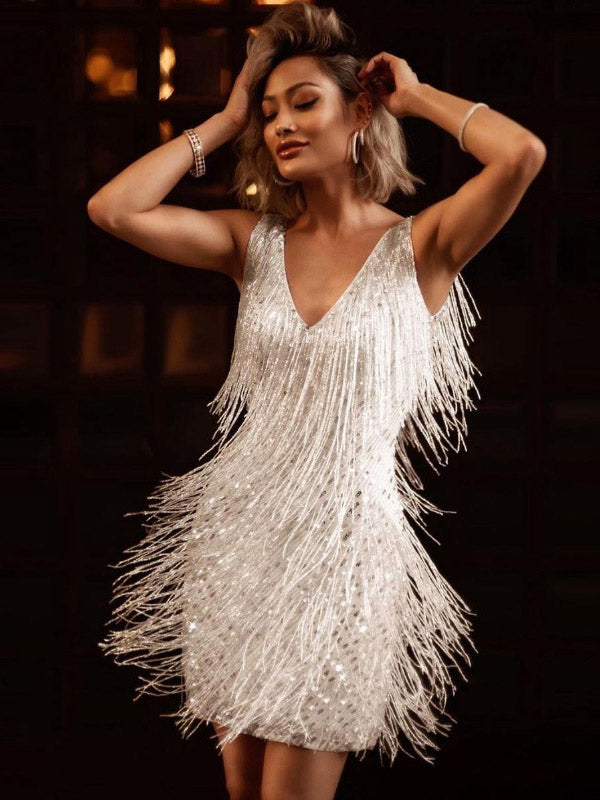 Woman in a white sequined fringe mini dress, posing with hands on head.