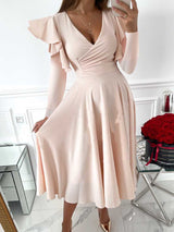 woman wearing a pale pink V-neck dress with ruffled long sleeves and a flared skirt