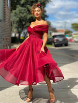Woman wearing a red off-the-shoulder A-line dress with a cinched waist and flared skirt, standing outdoors.