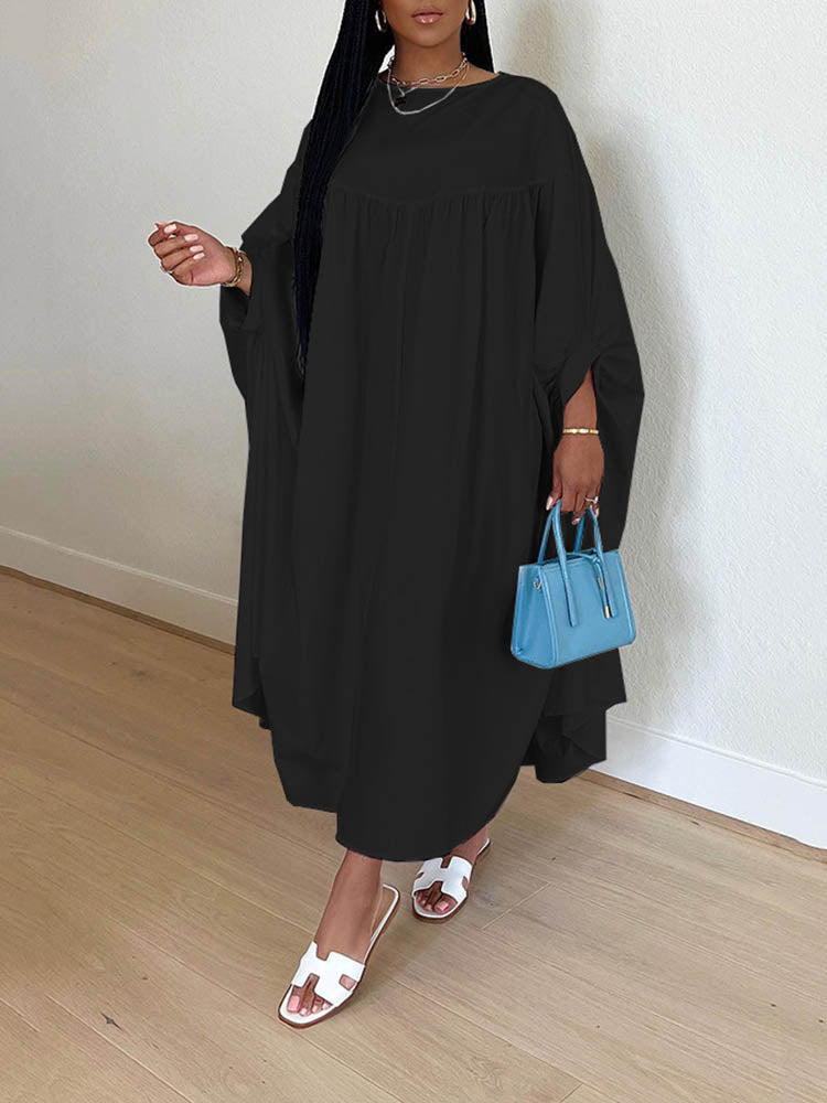 Woman wearing a black maxi dress with flowy sleeves and white sandals, holding a blue handbag