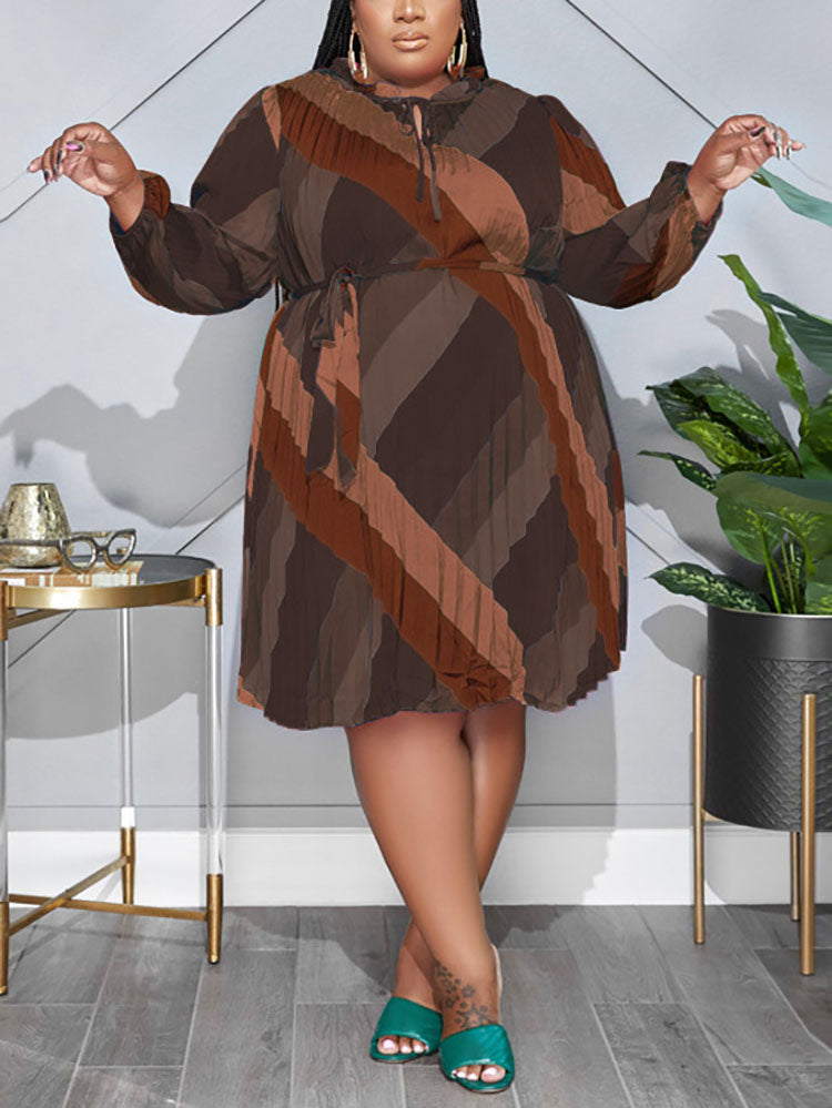 Plus-size woman wearing a brown, long-sleeved, pleated A-line dress with a geometric print and tie-waist.