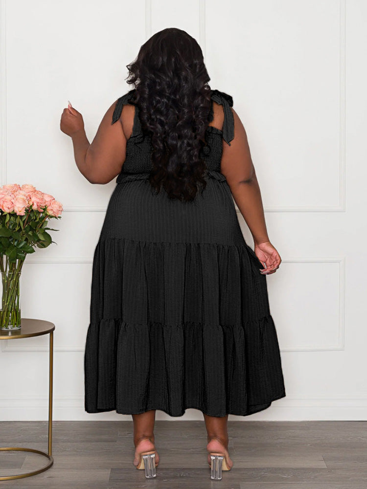 Back view of a plus-size woman wearing a black tiered maxi dress with tie shoulder straps and a smocked bodice.