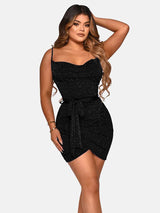 Woman wearing a short black sparkly dress with a cowl neckline and spaghetti straps, tied at the waist with a matching belt, against a white background.