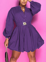 Woman in a purple fit and flare dress with balloon sleeves and a decorative belt, holding a black clutch.