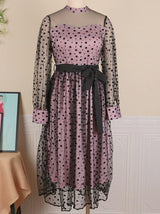 Pink and black polka dot midi dress with sheer long sleeves and a black ribbon belt, displayed on a mannequin.