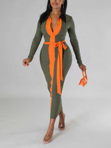 Woman wearing a long-sleeved olive green ribbed midi dress with contrasting orange panels and a matching waist tie.