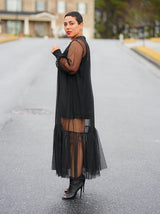 Side profile of a woman in a black sheer midi dress with a tiered hem.