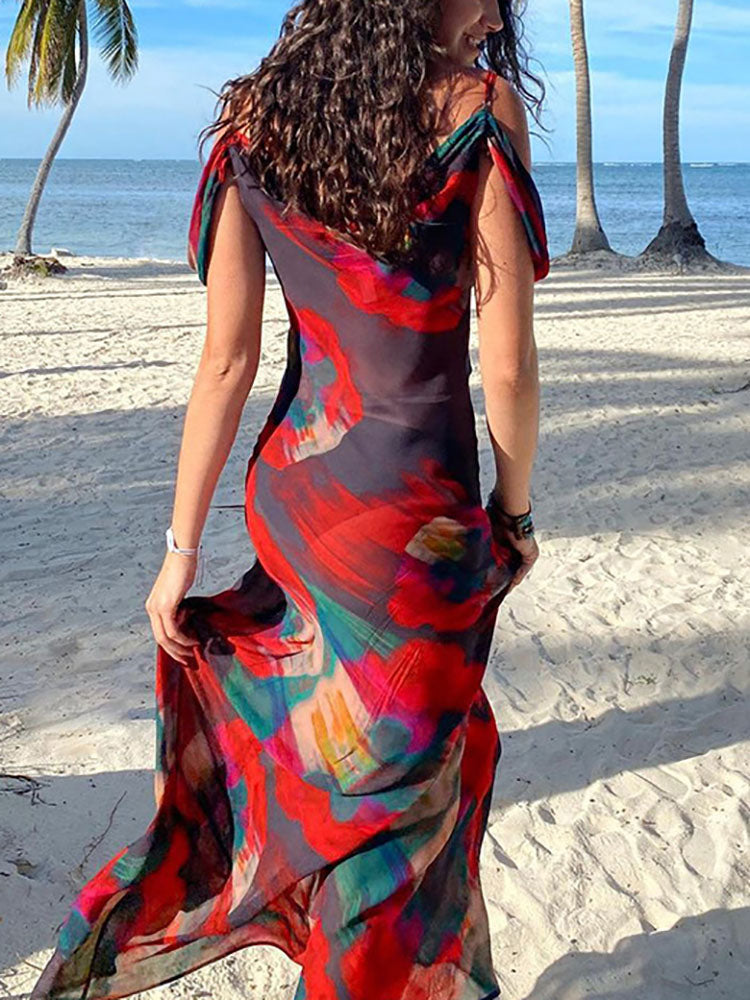 Rear view of a woman wearing a sheer abstract floral print maxi dress with cold shoulder sleeves on a sandy beach.