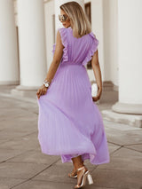 woman from behind wearing a long purple pleated dress with ruffled sleeves and a tie belt