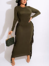 Woman wearing an olive green long-sleeved maxi dress with fringe detailing and a green handbag.