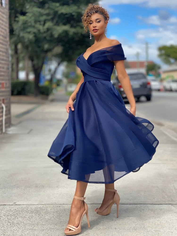 Woman wearing a navy blue off-the-shoulder A-line dress with a cinched waist and flared skirt, standing outdoors.