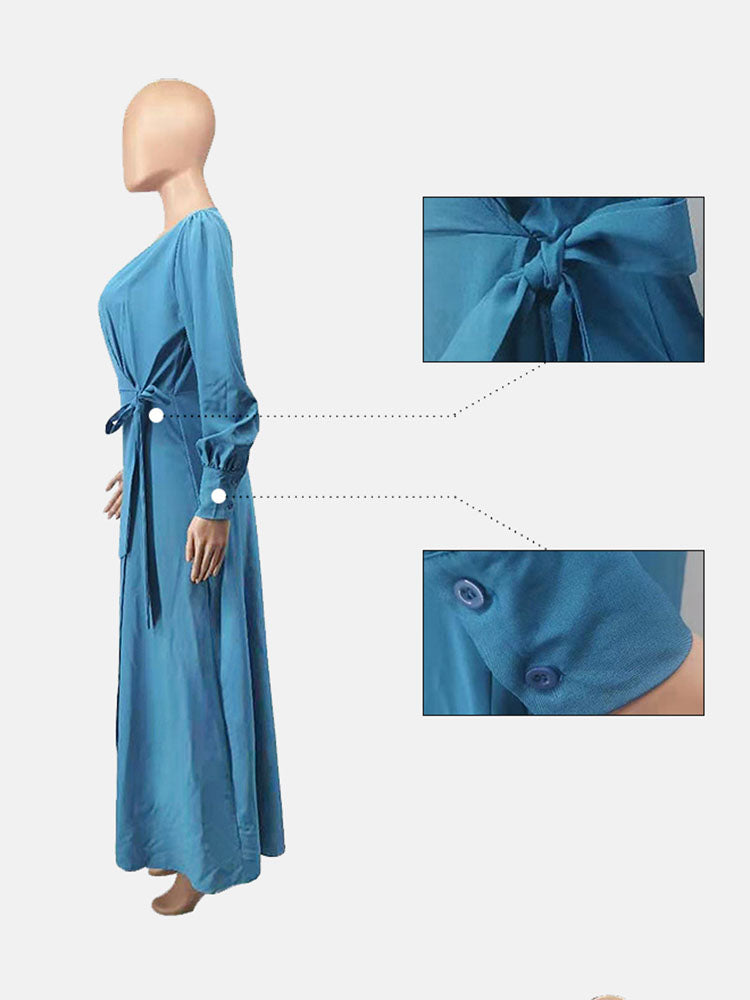 Side view of a woman wearing a teal long-sleeve maxi dress with a belted waist and high slit