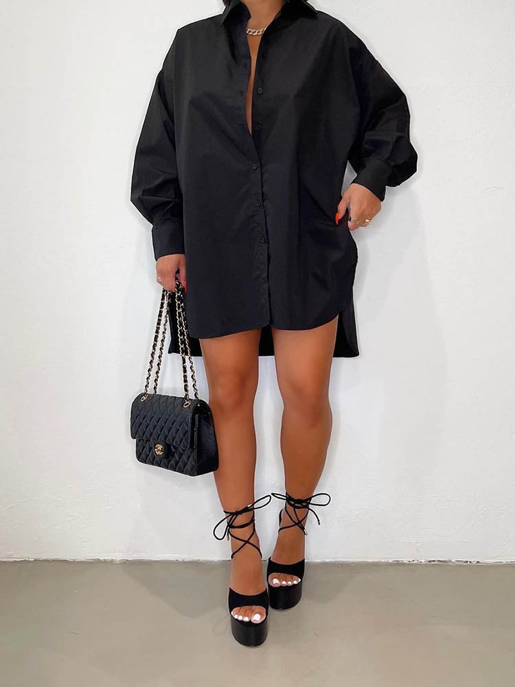 Woman wearing an oversized black collared shirt dress with a high-low hemline, paired with black platform heels and a black quilted handbag.