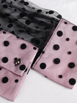 Close-up of the cuff of a pink and black polka dot dress with sheer sleeves.