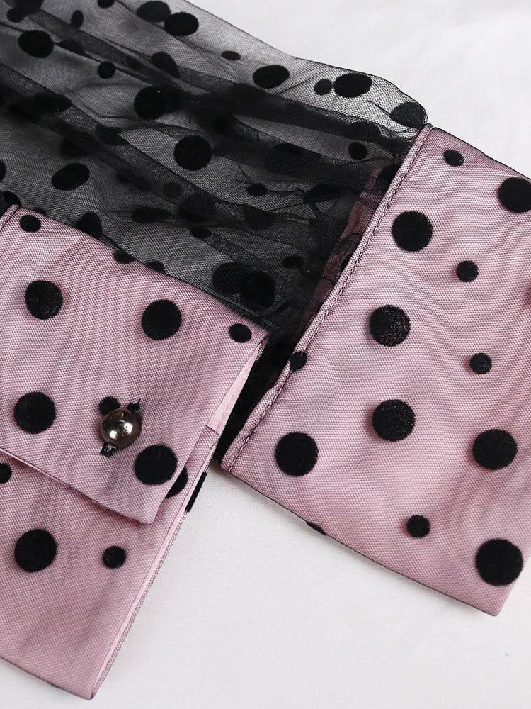 Close-up of the cuff of a pink and black polka dot dress with sheer sleeves.