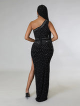 Woman wearing a black one-shoulder maxi dress with a high slit and rhinestone embellishments, back view