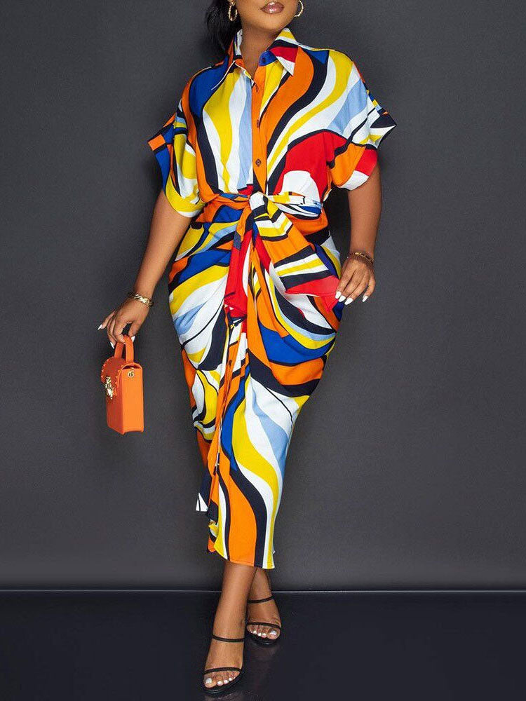 Woman wearing a colorful abstract print shirt dress with a tie waist and short sleeves.