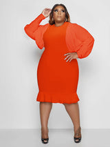 Woman in an orange dress with puff sleeves and a ruffle hem, posing with hand on hip.