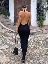 woman wearing a black backless maxi dress with a halter neckline, walking on a cobblestone path