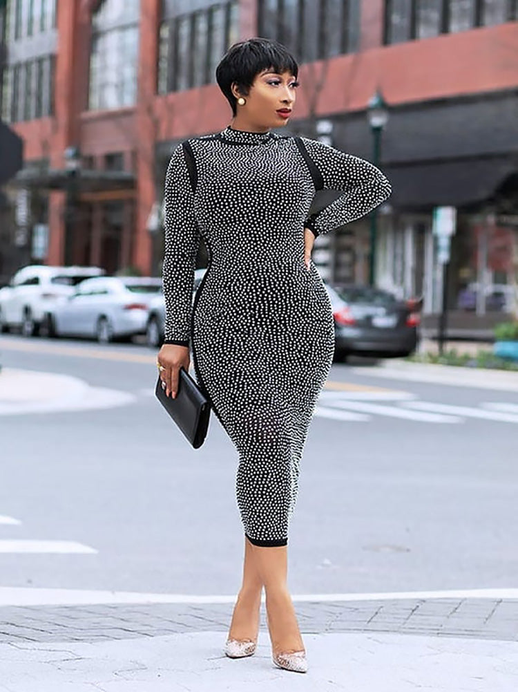 Woman wearing a black rhinestone midi dress and holding a black clutch.