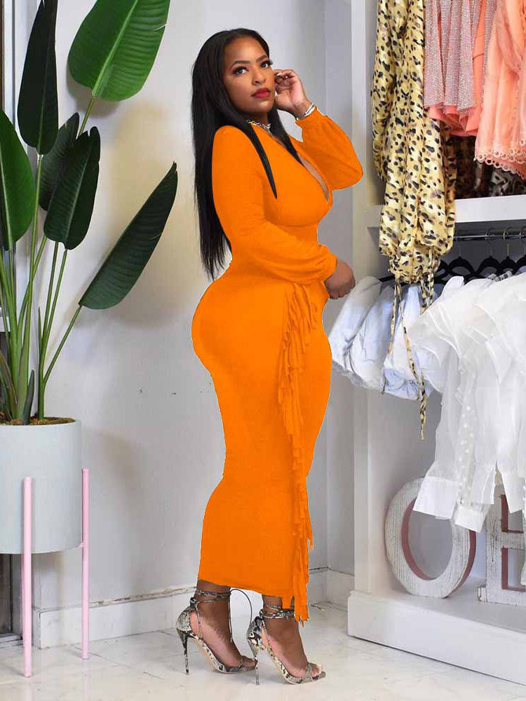Side view of a woman in an orange maxi dress with fringe detailing.