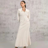 Woman wearing a cream-colored long-sleeved knit dress with a collared neckline, button-up front, dual chest pockets, and a flared hem, standing against a textured wall.