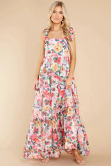 Woman wearing a floral print maxi dress with tie shoulder straps, standing against a plain background.