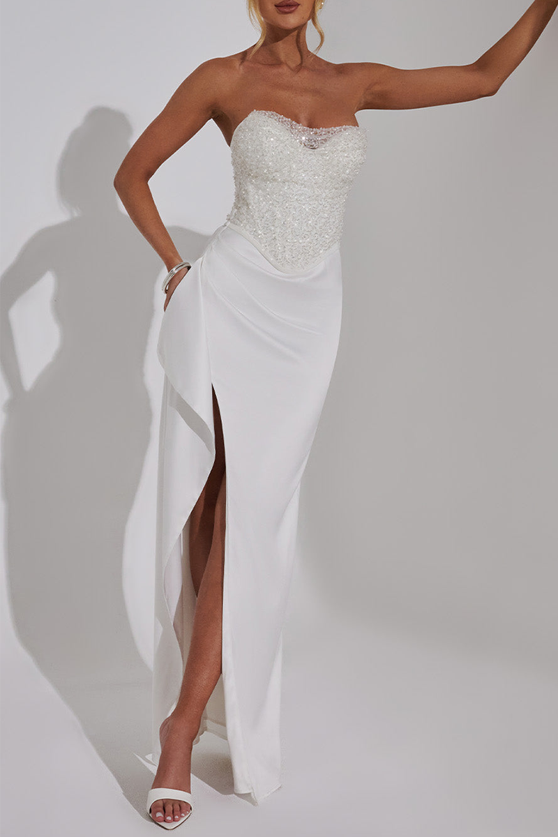 Woman wearing a white strapless evening gown with a high slit and embellished bodice against a white background